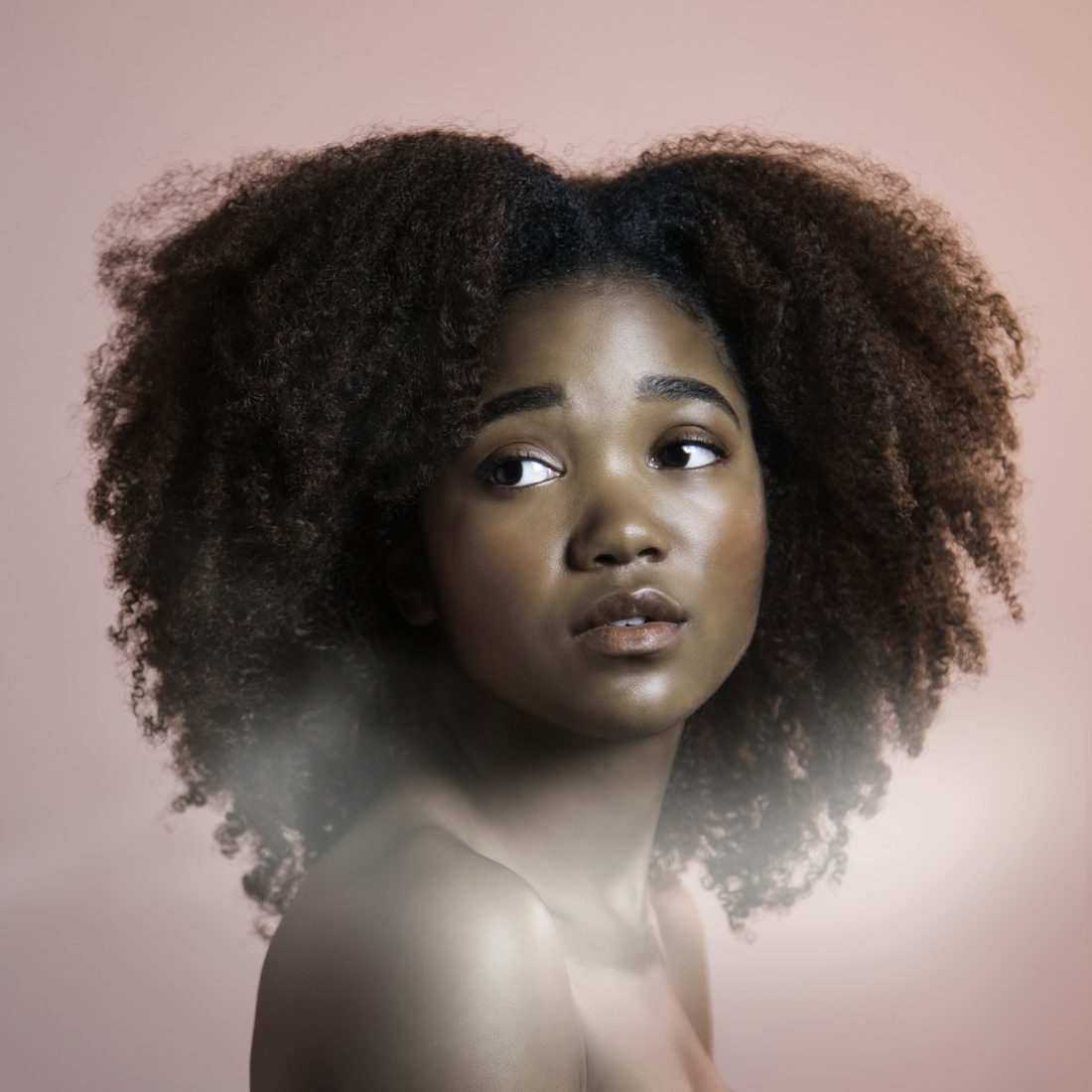 Portrait of a woman with full, natural curls against a blush background
