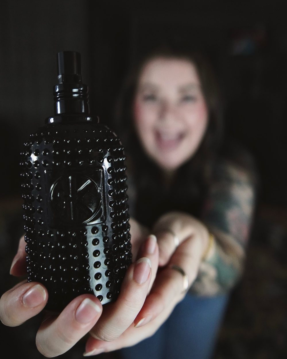 Sara smiling behind a black styling product bottle held to the camera