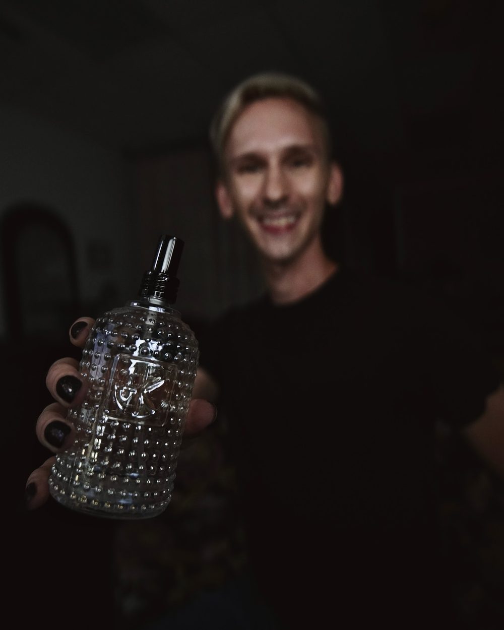 Skylar smiling and holding a clear styling product bottle toward the camera