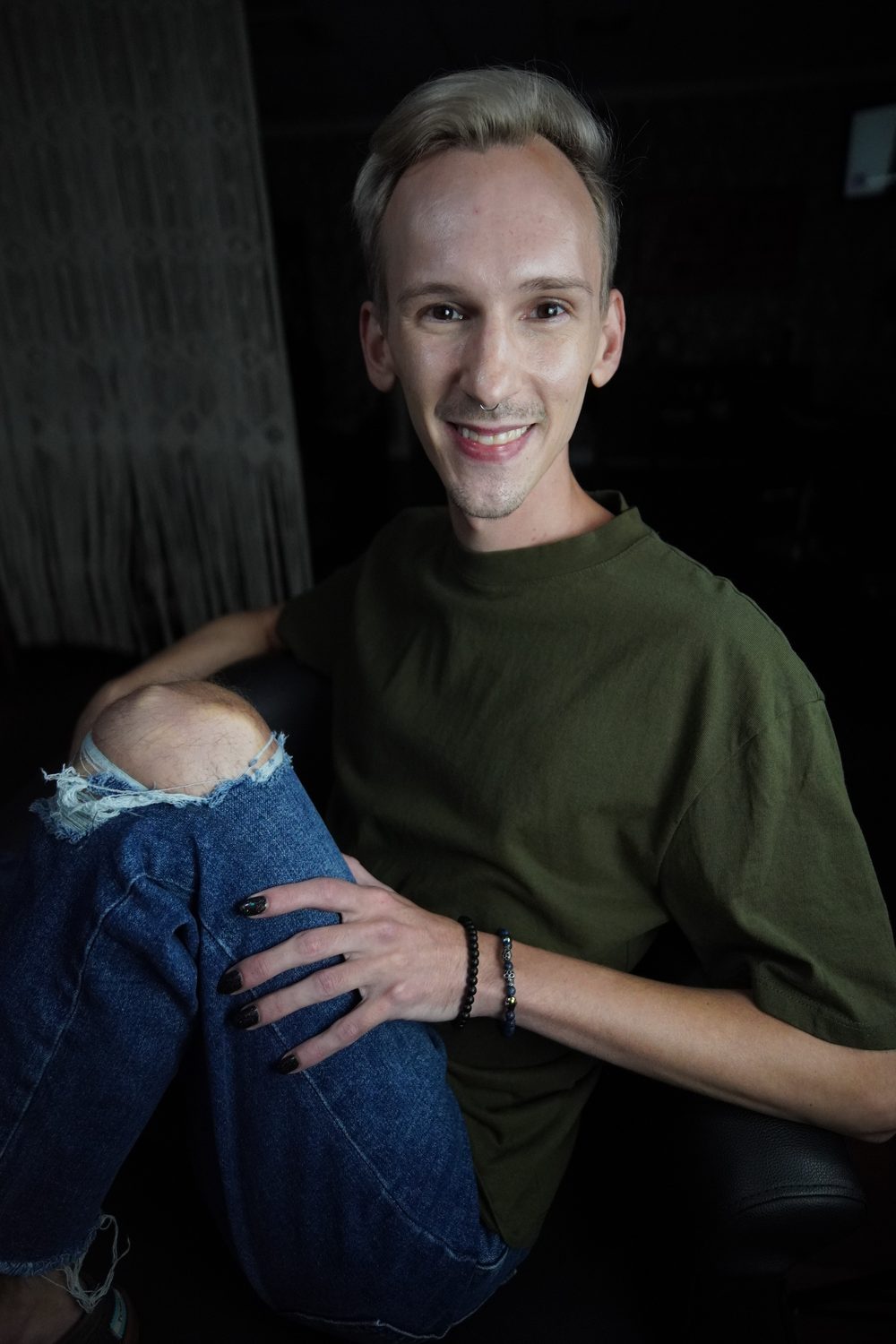 Skylar Johnson smiling in the suite, olive shirt and ripped jeans