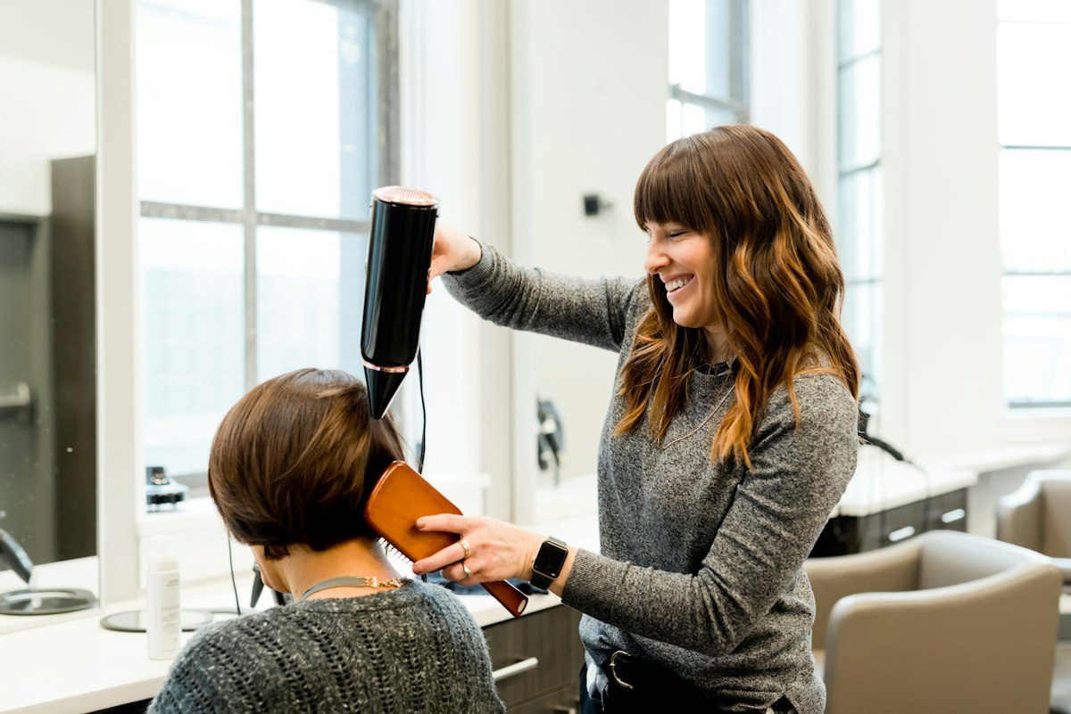 A stylist blow drying a client's hair in a bright salon