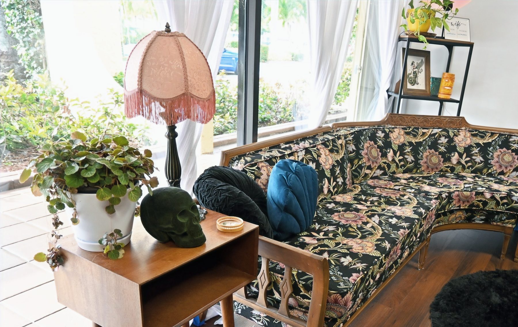 Inside the Worth Dyeing For suite, a vintage floral couch beside a blush fringe lamp and leafy plants